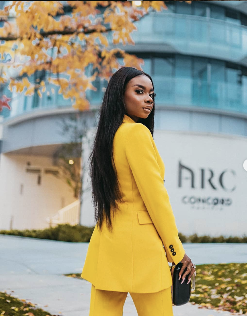 A lady in a yellow suit with long hair holding a purse