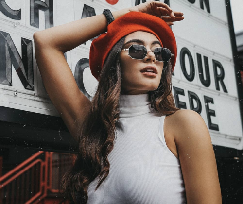 A lady next to a signpost wearing a white sleeveless pull neck top, a red hat and sunglasses